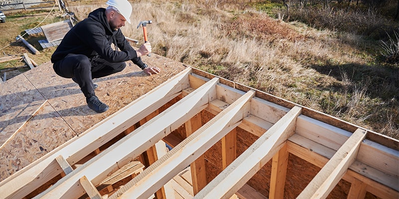 builder hammering nails onto roof